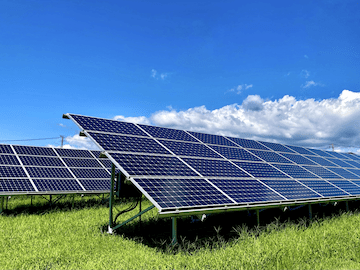 澄み渡った空の下、青々とした芝生の上に並ぶ太陽光発電のパネル。